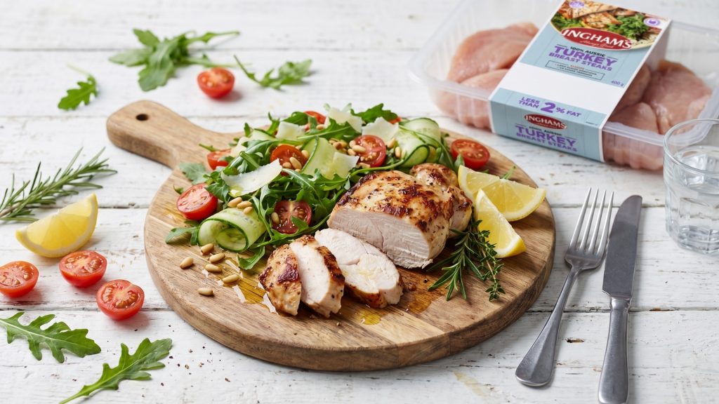 Sliced golden Ingham's turkey breast steak served on a wooden board with rocket, cherry tomatoes, cucumber ribbons, pine nuts and lemon wedges