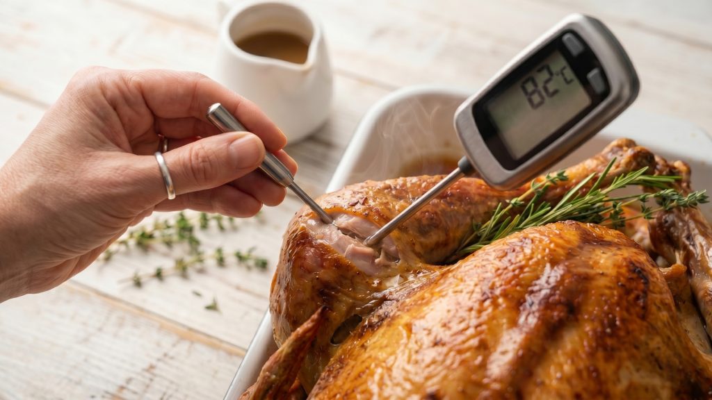 A meat thermometer being inserted into the thickest part of a roasted turkey thigh to check the safe internal temperature.